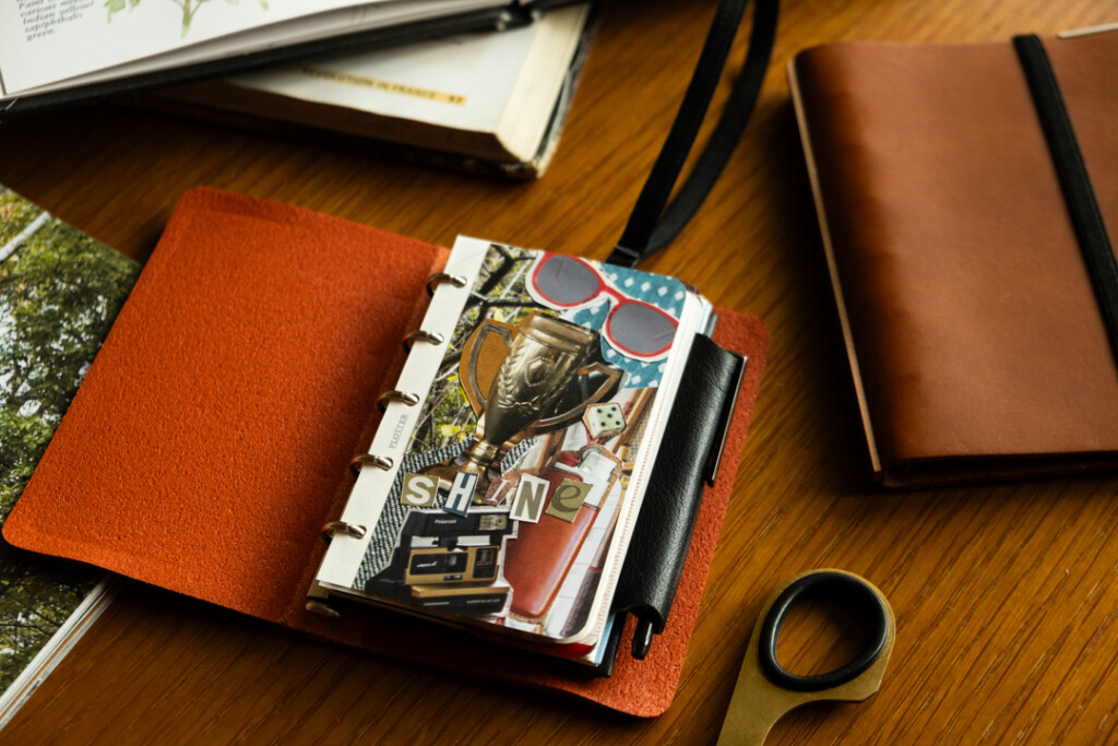 A PLOTTER Mini 5 Size Leather Binder open to a a vision board of images that relate to the owner's goals.