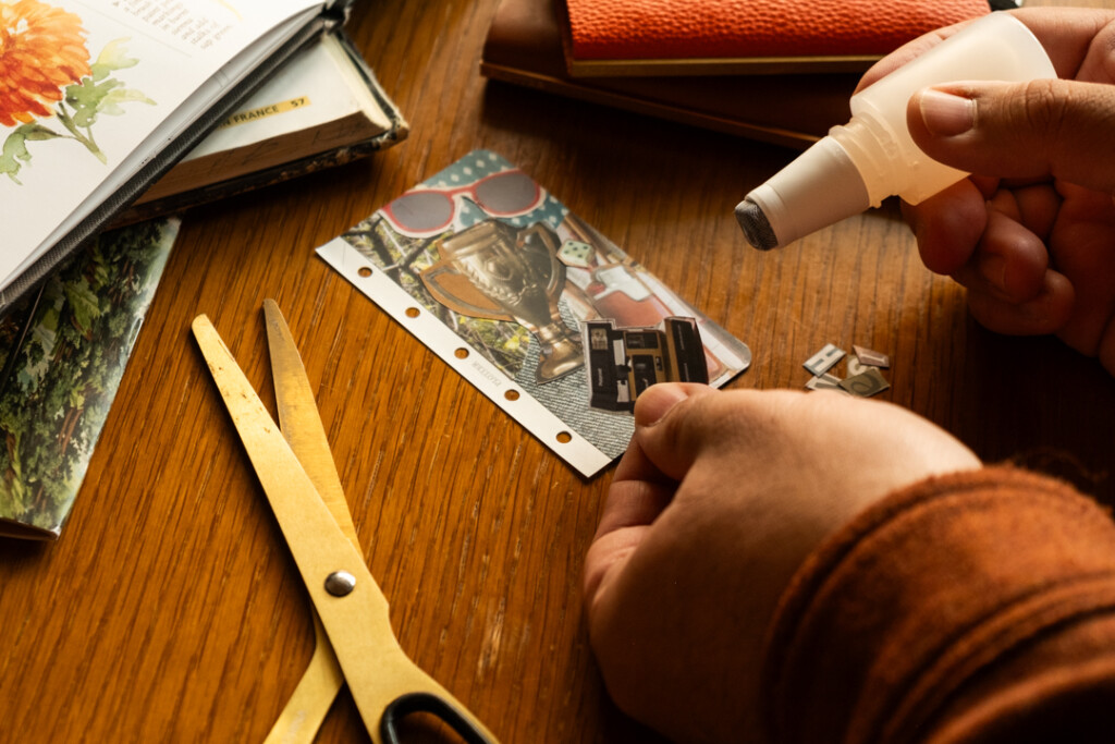 A person gluing a collage cutting into a vision board that fits into a PLOTTER Mini 5 Size Leather Binder.