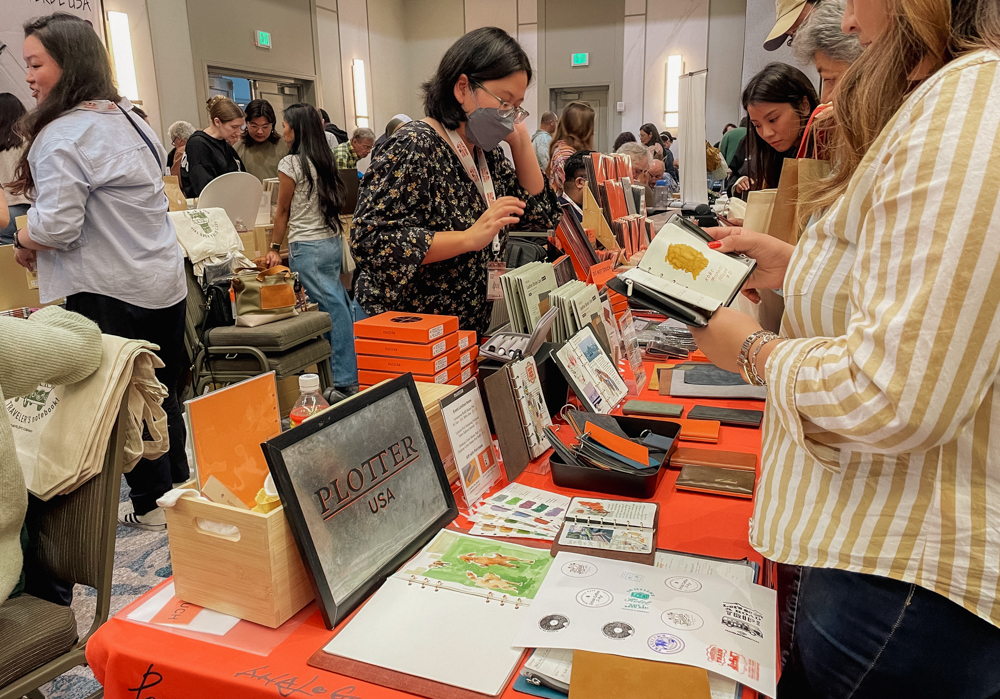 Person looking at PLOTTER items from the PLOTTER USA table at the California Pen Show.