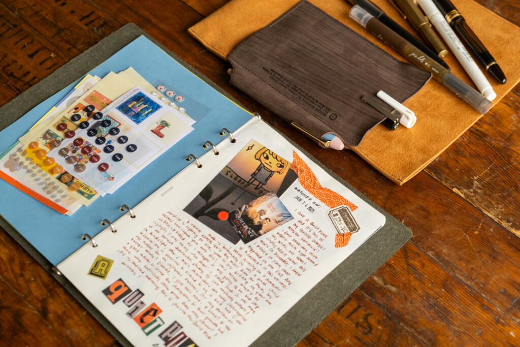 Close up of a PLOTTER Leather Binder A5 Size open to a mixed media TV show review journal page beside a Leather Binder Case in Yellow and Gray.