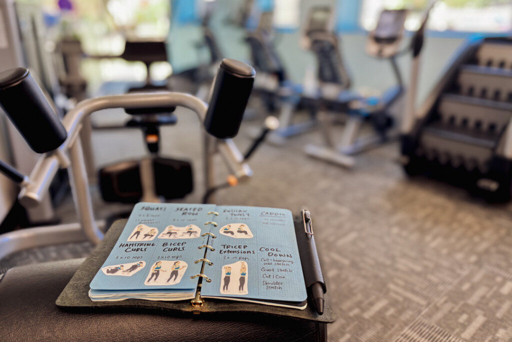A PLOTTER Mini Size open to a spread with a workout routine with images of the exercises in front of gym equipment.