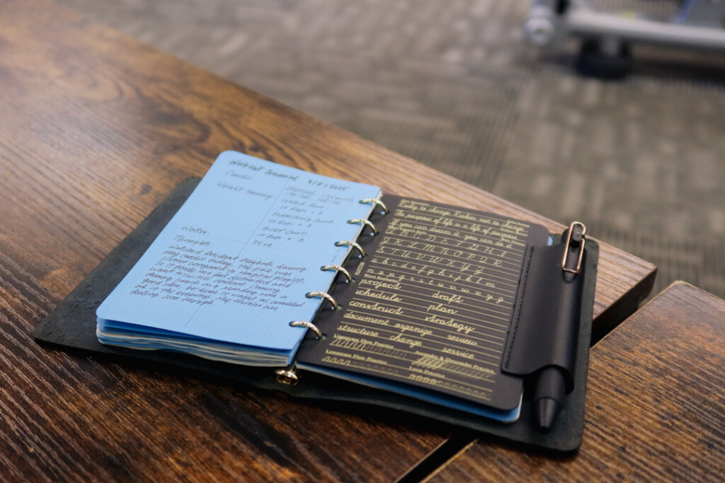A PLOTTER Mini Size at a table in the gym open to a spread with a workout routine.