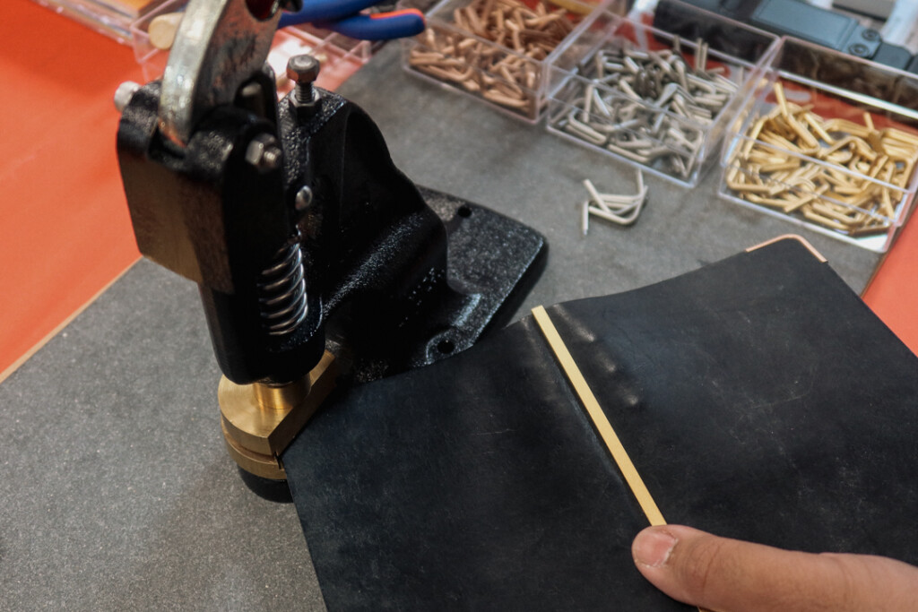 Close-up of the PLOTTER corner hardware customization machine being used to add corners to a black PLOTTER Leather Binder.
