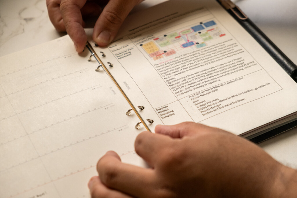 A person putting a printed sheet of A5 PLOTTER Paper into a PLOTTER Leather Binder and closing the ring mechanism.