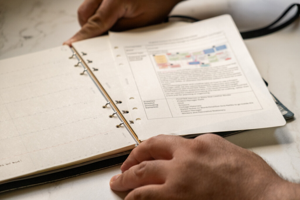 A person putting a printed sheet of A5 PLOTTER Paper into a PLOTTER Leather Binder.
