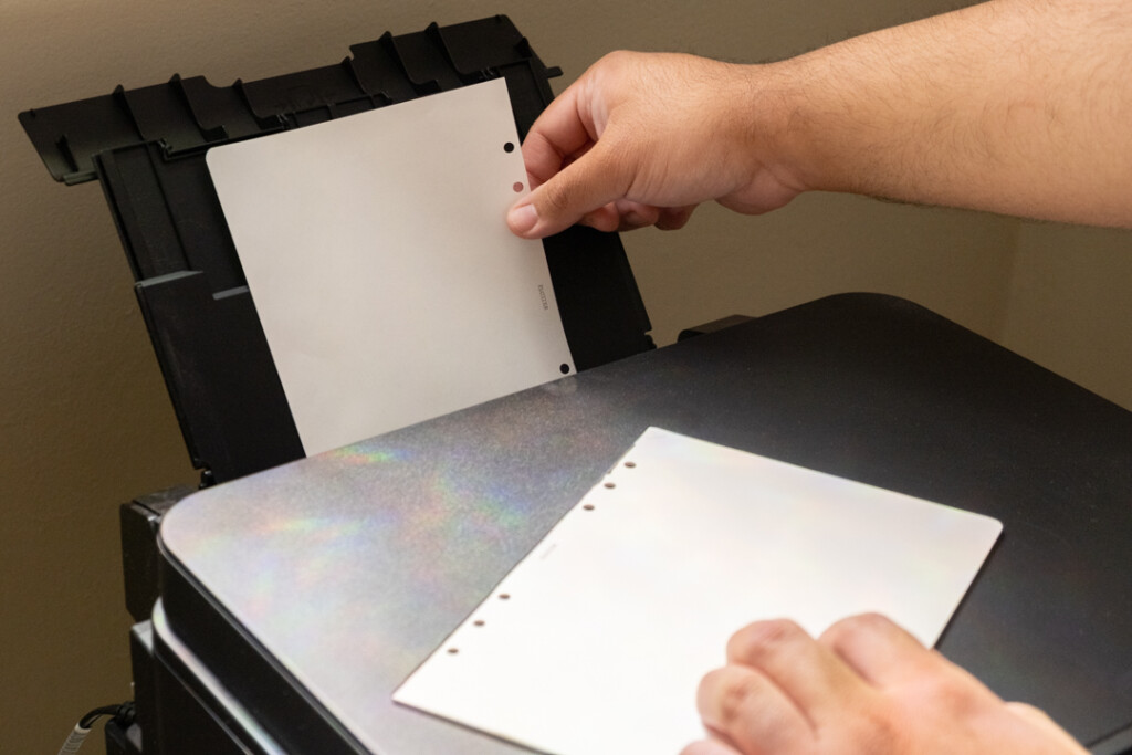 A person loading A5 size paper into the rear paper feed of a printer.
